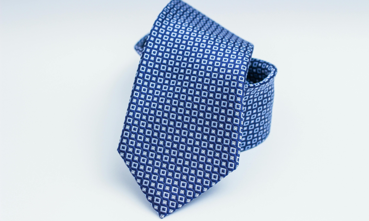 Blue geometric patterned silk tie with small square motif on neutral background