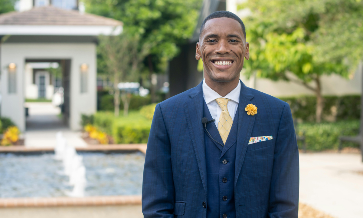 Man wearing navy suit with yellow tie and white shirt outdoors