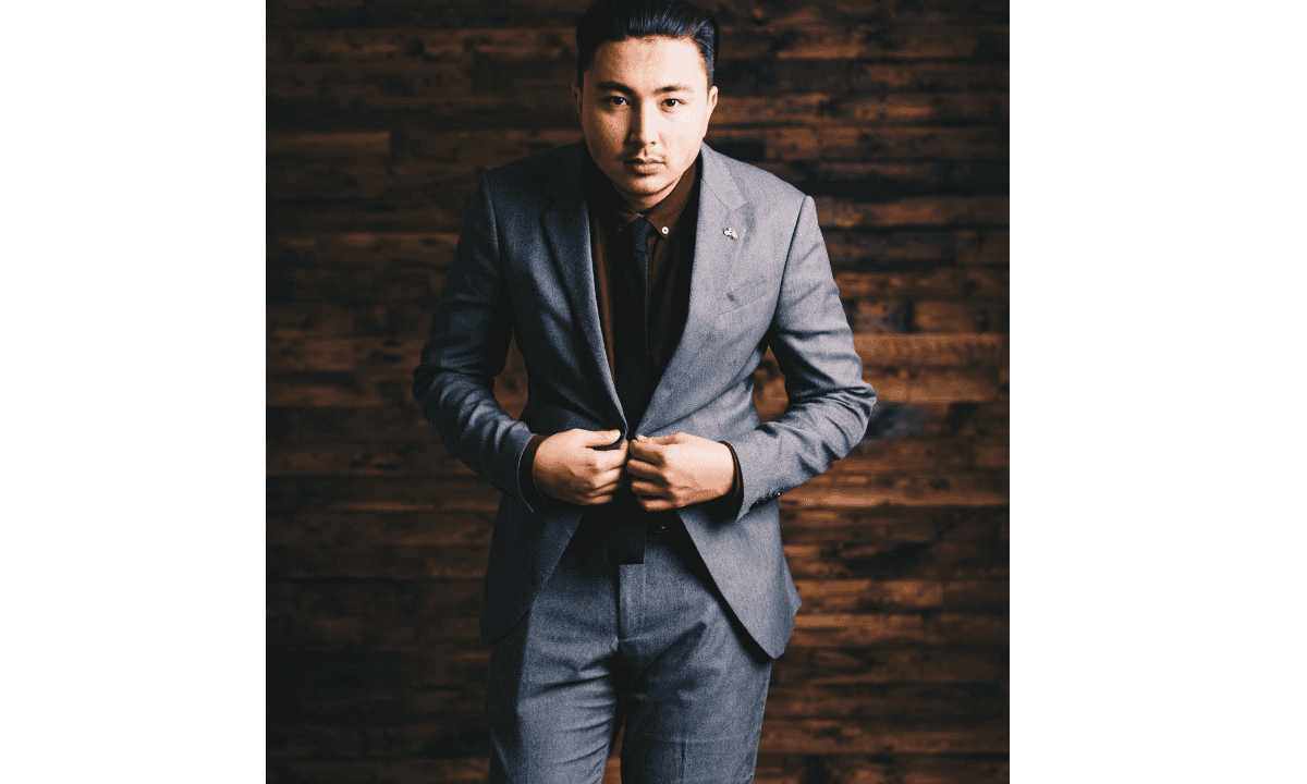 Man wearing tailored grey single breasted suit standing against wooden background