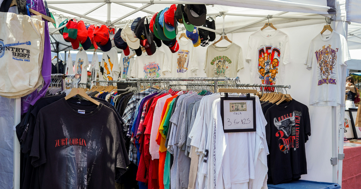 Clothing rack with graphic t shirts and hats displayed at an outdoor fashion market